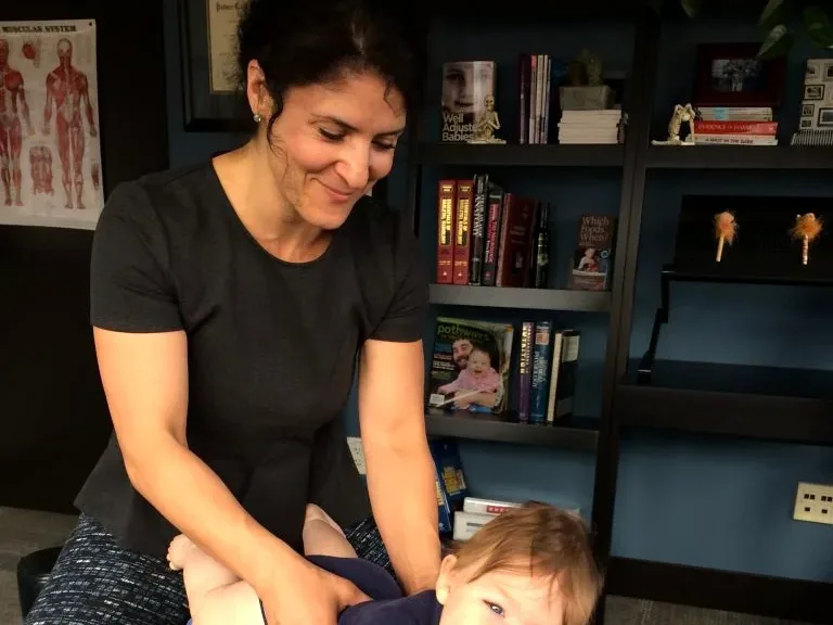 Dr. Xidos gently adjusting a smiling baby on a padded table