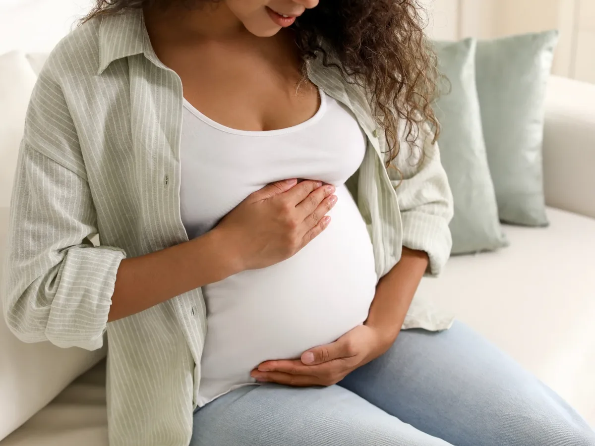 Pregnant woman sitting on a sofa with her hands resting on her belly
