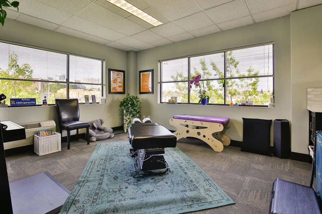 Bright adjusting room at Atlas Chiropractic with a chiropractic table and windows onto the trees
