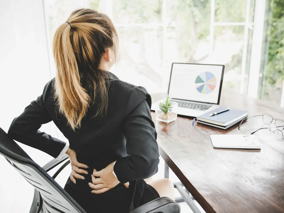 Woman at her desk pressing both hands into her lower back
