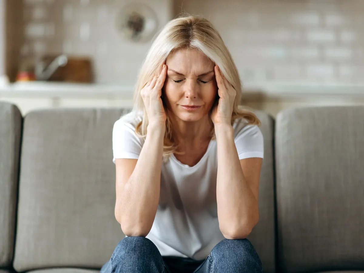 Woman on a sofa holding her temples with a headache